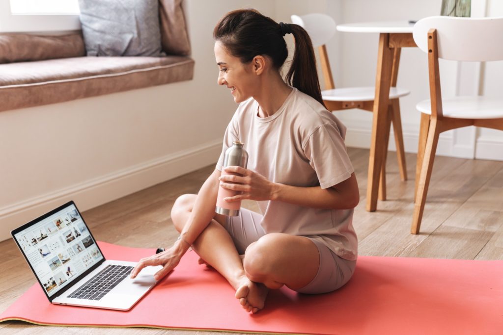 Fitness woman sit on rug using laptop computer
